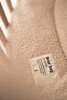 A close-up of a textured beige fabric with a label attached. Produktbild-Vorschau