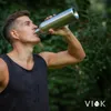 A man drinks from a stainless steel water bottle outdoors. Produktbild-Vorschau