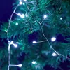 A close-up shot of a string of white LED lights on a dark green artificial Christmas tree. Produktbild-Vorschau