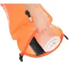 A hand is shown placing a rolled towel and a black object (likely a phone) into an open orange dry bag. Produktbild-Vorschau