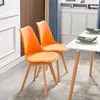 Two orange dining chairs are placed next to a white table in a room with blue curtains and wooden wall paneling. Voir les images du produit