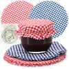 A jar of jam is decorated with a red and white checkered fabric lid and surrounded by matching fabric circles and white elastic bands. Produktbild-Vorschau