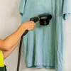 A person is using a handheld steam cleaner on a light blue t-shirt. Náhľad obrázku produktu