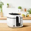A white air fryer sits on a wooden countertop in a kitchen setting with plants in the background. Produktbild-Vorschau