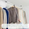 A person is using a telescoping pole with a hook to hang a jacket on a closet rod. Produktbild-Vorschau
