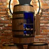A wooden barrel-shaped wine cabinet with a door open, displaying bottles of alcohol and wine, illuminated by blue LED lights, set against a brick wall. Produktbild-Vorschau