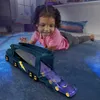 A young girl is playing with a toy truck and car on a blue carpet. Anteprima dell’immagine prodotto