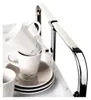 A close-up shot of stacked white mugs and saucers on a white surface, with a chrome handle of a serving cart in the background. Produktbild-Vorschau