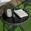 A small round table with a candle lantern and a book on it, placed on a green surface with wooden planks in the background. Produktbild-Vorschau
