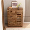 A wooden cabinet with drawers and a slatted door, placed in a room with a door and a wall with vertical lines. Podgląd zdjęcia produktu