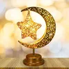 A decorative golden lamp shaped like a crescent moon holding a star, placed on a wooden surface with a bokeh background. Produktbild-Vorschau