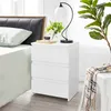 A bedside table with a lamp, flowers, and a drink next to a bed.