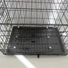 A close-up view of the bottom of a black wire dog crate with a black plastic tray. Náhled obrázku produktu