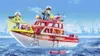 A Playmobil fire rescue boat with two figures on board, sailing on the water with a harbor in the background. Produktbild-Vorschau