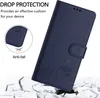 A dark blue flip case for a phone, with a cat design, is shown against a background of broken white pieces, suggesting drop protection. Produktbild-Vorschau