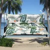 A swing cushion with a tropical leaf pattern is shown on a swing set on a beach with palm trees. Produktbild-Vorschau