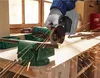 A person wearing gloves is using a cordless angle grinder to cut a metal rod clamped in a vise. Sparks are flying from the cutting action. Produktbild-Vorschau