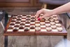 A hand is shown moving a checker piece on a wooden checkerboard. Podgląd zdjęcia produktu