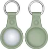 Two identical green keychains with silver rings are shown side-by-side against a white background. The left keychain displays the front of the device holder, which has a circular indentation for a tracker. The right keychain shows the back of the holder. Produktbild-Vorschau