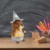 A plush toy marmot dressed in traditional Bavarian attire sits on a wooden surface in front of a chalkboard background. Nearby are a small shopping cart filled with colored pencils, a brown paper bag, and a gift-wrapped box. Produktbild-Vorschau
