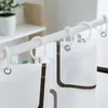A close-up view of a white shower curtain with a brown decorative border, hanging from a white shower rod with white rings. Produktbild-Vorschau