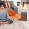 A woman meditates in front of a space heater in a living room. Voir les images du produit