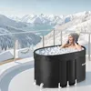 A woman is sitting in an ice bath on a balcony with a snowy mountain landscape in the background. Náhled obrázku produktu