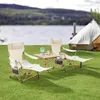 Camping scene with chairs, table, and tent by a lake. Produktbild-Vorschau