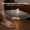 A person's foot wearing a pink slipper is shown next to a bed with a motion-activated light attached to the bed frame. Náhled obrázku produktu