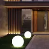 Two illuminated spherical garden lights are placed on a lawn in front of a modern house entrance. Produktbild-Vorschau