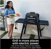 A woman is holding a tray of vegetables next to an electric grill on a stand. Voir les images du produit