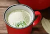 A close-up of a red mug filled with broth and herbs. Produktbild-Vorschau