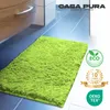 A fluffy green bath mat is placed on a tiled floor next to a cabinet. Anteprima dell’immagine prodotto