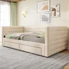 A beige upholstered daybed with two drawers is shown in a room with artwork on the wall and a window with green curtains. Náhled obrázku produktu