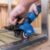 A person is using a blue and black rotary tool with a sanding attachment on a wooden surface with metal trim. Produktbild-Vorschau