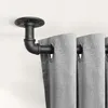 A close-up view of a black pipe curtain rod bracket attached to a white ceiling, holding a gray curtain. Produktbild-Vorschau