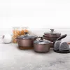 A set of rose gold cookware is displayed on a countertop with jars of food in the background. Náhled obrázku produktu