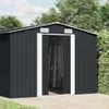 A dark gray metal shed with white trim and open doors, set against a backdrop of green trees and a cloudy sky. The shed is situated on a paved patio. Náhled obrázku produktu