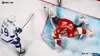 A hockey player in a white jersey with the number 59 on it is skating towards the goal, while the goalie in a red jersey dives to make a save. The game is being played on an ice rink. Produktbild-Vorschau