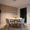 A modern dining room with a round wooden table set for a meal, illuminated by a sleek LED pendant light. Produktbild-Vorschau