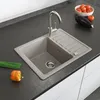 A kitchen sink with a faucet and a drying rack, along with some vegetables and chives on a countertop. Anteprima dell’immagine prodotto