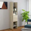 A tall, narrow bookshelf with two drawers and several shelves, filled with books and decorative items, stands against a light gray wall next to a large potted plant and a blue armchair. Produktbild-Vorschau