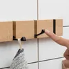 A hand is shown pressing on a fold-down hook of a wooden wall-mounted coat rack, with a towel hanging from another hook. Produktbild-Vorschau