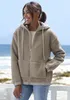 A woman wearing a fleece jacket stands on a beach with the ocean in the background. Produktbild-Vorschau