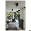 A modern living room with large windows overlooking a garden, featuring furniture and lighting. Produktbild-Vorschau