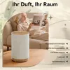 A woman reading a book on a couch next to an aroma diffuser, with a bed in the background. Produktbild-Vorschau