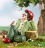 A garden gnome clown sitting on a tree stump with a bird on its knee, with a birdhouse in the background. Produktbild-Vorschau
