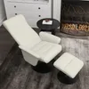 A white recliner chair with a matching ottoman is shown in a living room setting, next to a fireplace and a small side table. Produktbild-Vorschau