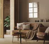 A cozy living room scene with a brown leather sofa, armchair, and coffee table, decorated with pillows and a blanket. A large plant is visible in the background. Produktbild-Vorschau