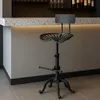 A black industrial-style bar stool with a tractor seat and footrest is shown in front of a bar counter. Voir les images du produit